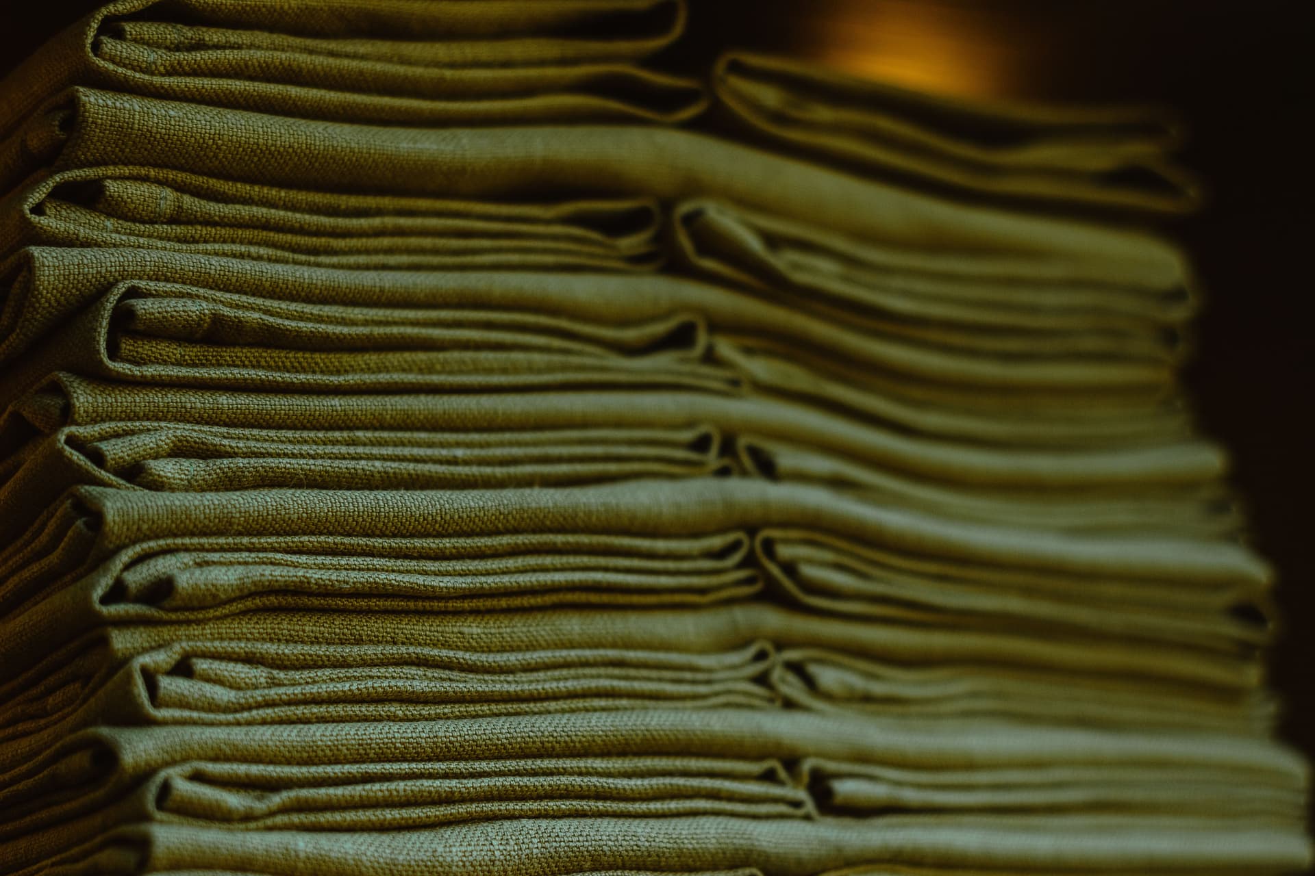 Close-up of a stack of neatly folded green linens, showing the texture of the cloth and the edges of each fold.